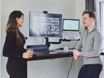 Colleagues speaking at desk, with single monitor arm holding laptop and screen behind them.